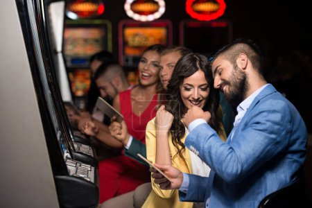Schöne und gut gekleidete Freunde spielen Automaten im Casino und feiern