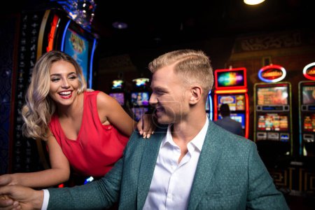 Schöne und gut gekleidete Freunde spielen Automaten im Casino und feiern