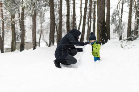 Photo for Joyful Boy in Warm Clothes Happily Playing With Mother in Snow Outdoors During Snowfall - Royalty Free Image
