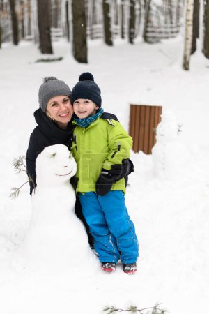 Photo for Joyful Boy in Warm Clothes Happily Playing With Mother in Snow Outdoors During Snowfall - Royalty Free Image