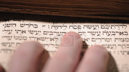Téléchargez les photos : Fingers on page of old book Torah. Selective focus on snippet Hebrew Bible text that translates in english: offer the Passover sacrifice to Jehovah. Closeup - en image libre de droit