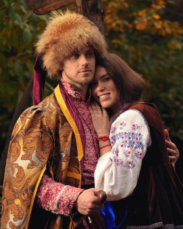 Photo for Young happy couple dressed traditional ukrainian clothing. Serious cossack man and smiling woman in embroidered costumes outdoors. Vintage outfit - Royalty Free Image