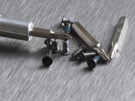 Schrauben und Ersatzbits für einen Schraubenzieher auf grauem Metallhintergrund Nahaufnahme