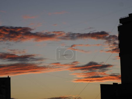 Coucher de soleil entre les gratte-ciel qui sont reliés par des fils de la métropole parmi les nuages orange-noir