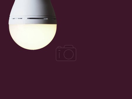 Eine eingeschaltete LED-Akku-Lampe in den Händen einer Person auf weinrotem Hintergrund