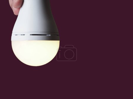 Una lámpara led recargable encendida en las manos de una persona sobre un fondo borgoña