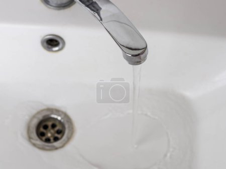 Faucet with water, metallic shine, white sink