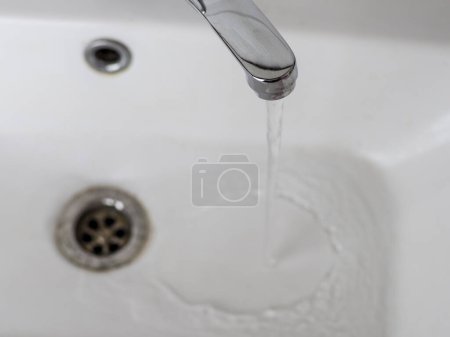 Faucet with water, metallic shine, white sink