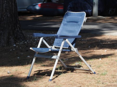 A blue folding chair among nature and cars