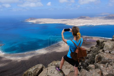 Foto de Mujer excursionista fotografiando con su teléfono inteligente desde lo alto de una colina La Graciosa Island. Islas Canarias - Imagen libre de derechos