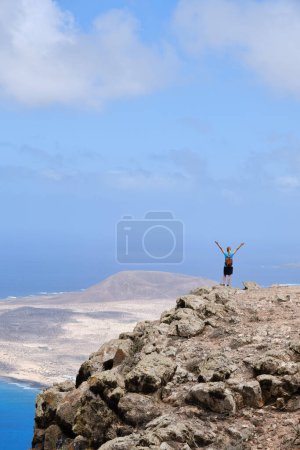 Foto de Mujer de pie con los brazos levantados en la cima de una colina. Con La Graciosa al fondo - Imagen libre de derechos