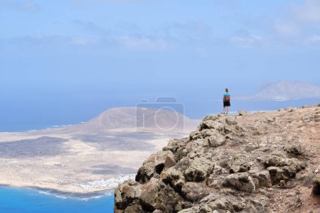 Foto de Caminante admirando el paisaje desde una colina, La Graciosa Island en el fondo. - Imagen libre de derechos