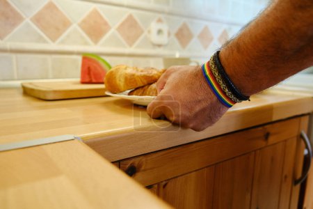 Crop main anonyme de plaque de maintien mâle avec croissant frais au comptoir en bois dans la cuisine pendant la préparation du petit déjeuner à la maison