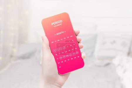 Foto de Mujer sosteniendo el teléfono móvil con aplicación de calendario de ciclo menstrual en el fondo de la habitación blanca. diseño de aplicación rosa - Imagen libre de derechos