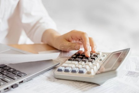 Photo for Female hands doing accounting calculations using a calculator. utility services. papers invoices cheque bills, female hands holding receipt calculating company expenses results of incomes - Royalty Free Image