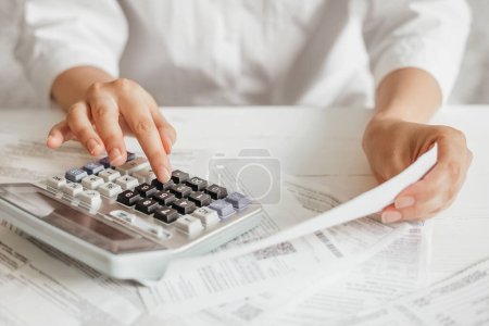 Téléchargez les photos : Female hands doing accounting calculations using a calculator. utility services. papers invoices cheque bills. accountant conducts calculations, pays and closes accounts - en image libre de droit