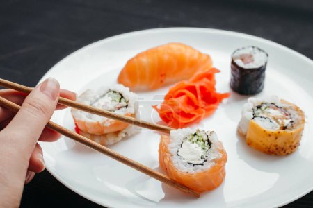 Different types of sushi rolls on white plates on black background top view