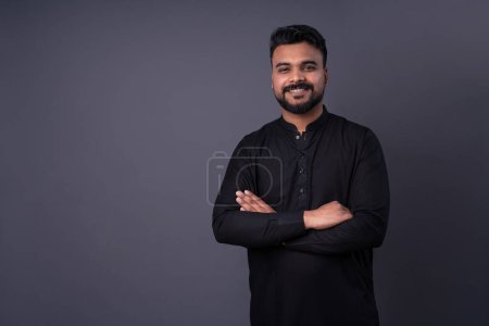 Photo for Happy smiling man looking at camera. Pakistani young man in traditional black shirt clothes. Man with dark hair, mustache beard. arms crossed. - Royalty Free Image