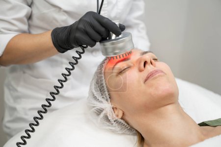 Photo for Infra red lights tool. Professional disinfection cosmetology. Relaxed patient young woman  with closed eyes during procedure. Modern cosmetology anti aging skin care - Royalty Free Image