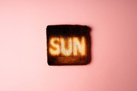 Photo for Dark burnt slices of white bread toast with the word Sun on it on pink background. passionate Sunbathing. creative concept composition representation danger of sun radiation and photo aging - Royalty Free Image