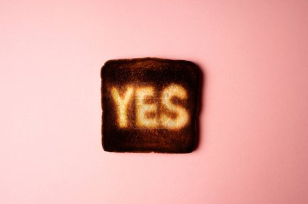 Photo for Burnt dark slice of white bread toast with the word Yes on it on pink background passionate ardent agreement. poster creative concept composition - Royalty Free Image