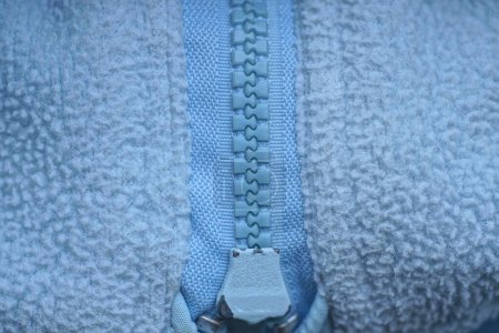 Foto de Textura de una parte de una cremallera cerrada de plástico con dientes azules en una tela gris de ropa - Imagen libre de derechos