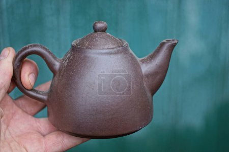 Foto de Mano sosteniendo una vieja tetera de cerámica marrón sobre un fondo verde - Imagen libre de derechos