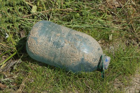 Photo for Garbage from one big closed blue plastic bottle in gray mud on green grass in nature - Royalty Free Image