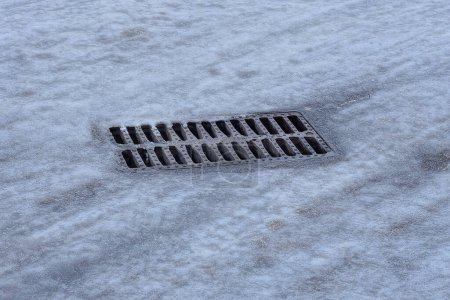 Photo for One rectangular gutter from an iron brown grate on a road in gray ice on a winter street - Royalty Free Image