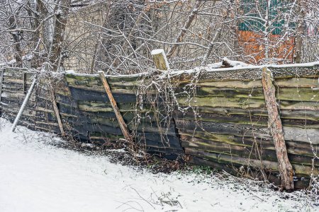 Foto de Parte de una vieja cerca gris de madera negra en nieve blanca en una calle rural de invierno - Imagen libre de derechos