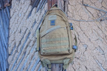 Photo for One big green tactical army backpack hanging on a brown clay wall in the street - Royalty Free Image