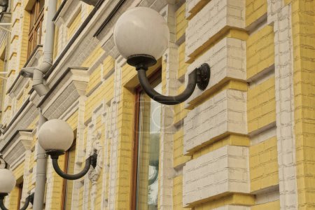 Téléchargez les photos : Lanterns from white round glass shades hang on a yellow brick wall of a building with windows on the street - en image libre de droit