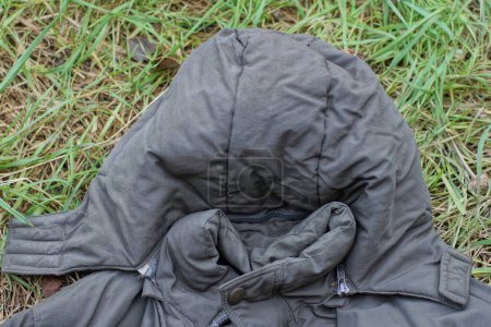 Téléchargez les photos : One gray fabric hood from a winter jacket lies on the green grass on the street - en image libre de droit