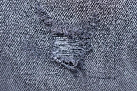 Photo for A piece of gray black denim pants with threads on torn fabric - Royalty Free Image