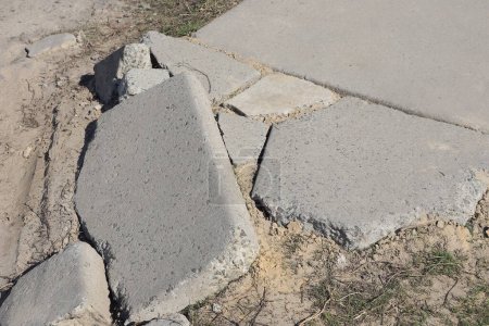 part of the road with broken gray concrete slabs with cracks in the sand on the street