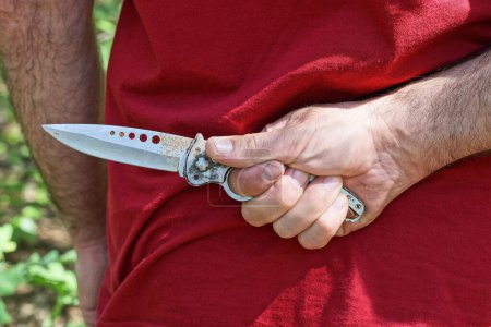 Foto de Un hombre con ropa roja sostiene un cuchillo gris detrás de su espalda - Imagen libre de derechos