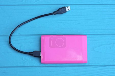 Photo for One pink plastic drive and a black usb cable lies on a blue wooden table - Royalty Free Image