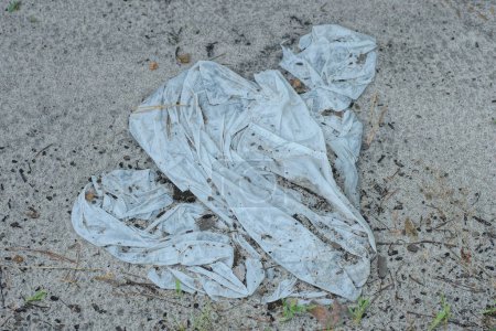 Téléchargez les photos : Ordures d'un sac en plastique blanc froissé se trouve sur du sable gris dans la rue - en image libre de droit