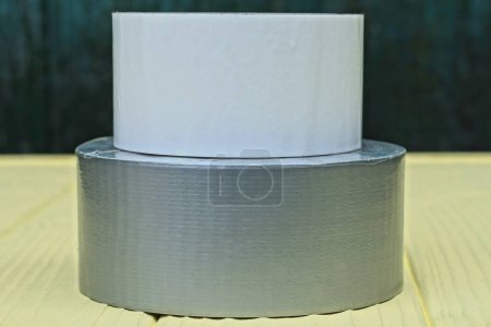 Foto de Un rollo de cinta gris reforzada y un rollo de cinta blanca yacen sobre una mesa de madera amarilla - Imagen libre de derechos