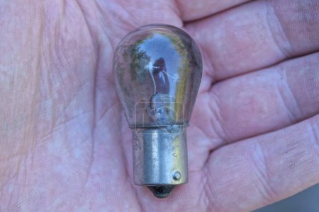 Foto de Una pequeña bombilla de luz negra gris eléctrica de vidrio quemado yace en la palma de su mano - Imagen libre de derechos