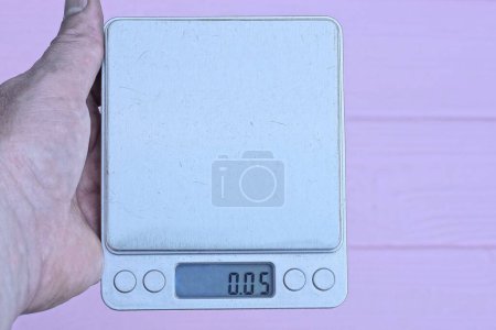 Foto de Mano sosteniendo una balanza electrónica cuadrada gris sobre un fondo rosa - Imagen libre de derechos