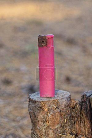 Téléchargez les photos : Un vieux briquet rose en plastique se tient sur une souche de bois gris dans la rue - en image libre de droit