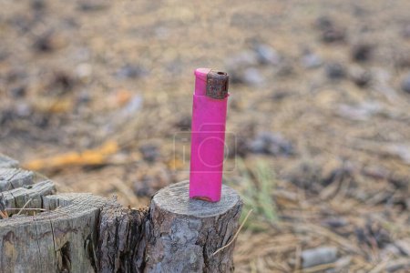 Téléchargez les photos : Un vieux briquet rose en plastique se tient sur une souche de bois gris dans la rue - en image libre de droit