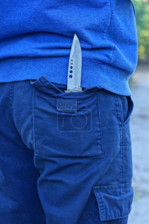 Foto de Un cuchillo de hierro afilado gris en un bolsillo azul de los pantalones del hombre en su pierna en la calle - Imagen libre de derechos
