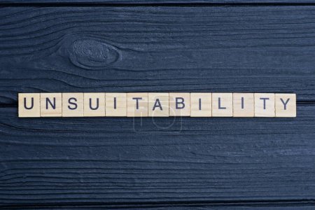 Photo for Text the word unsuitability from brown wooden small letters on a black table - Royalty Free Image