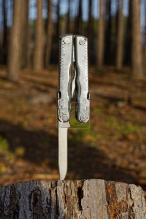 Photo for One white metal multitool with a knife and an iron blade sticks out in a gray stump on the street - Royalty Free Image