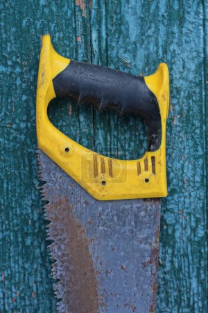 Photo for One old rusty metal hacksaw with a plastic yellow black handle stands against a green wall - Royalty Free Image