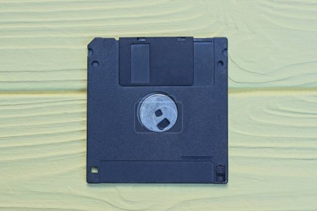 Téléchargez les photos : Une vieille disquette d'ordinateur en plastique carré noir repose sur une table en bois jaune - en image libre de droit
