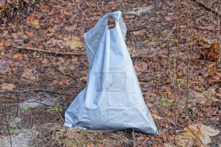 Téléchargez les photos : Un grand sac en plastique gris déchiqueté avec des ordures debout sur le sol brun dans la rue - en image libre de droit