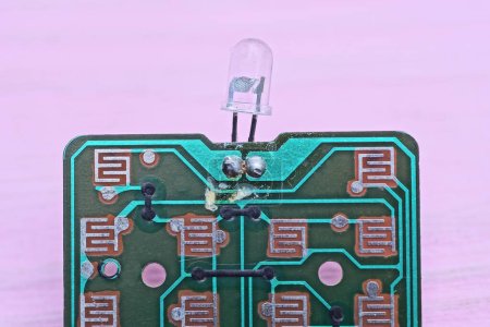 one green old plastic microcircuit with small LED bulb with lead soldering lies on a pink table